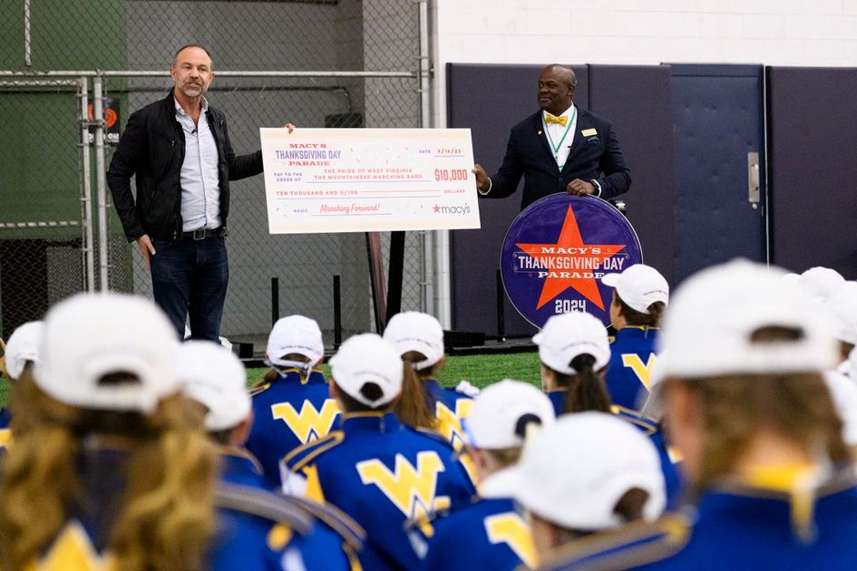 Wesley Whatley, Macy’s Thanksgiving Day Parade creative producer, surprises members of the Mountaineer Marching Band with an invitation to march in the 2024 parade on Saturday (Sept. 16) at the Caperton Indoor Practice Facility. Cheldon Williams (right), WVU associate director of bands and director of athletic bands, accepted $10,000 to kick off fundraising for the trip through the Pride Travel Fund. (WVU Photo/Matt Sunday)