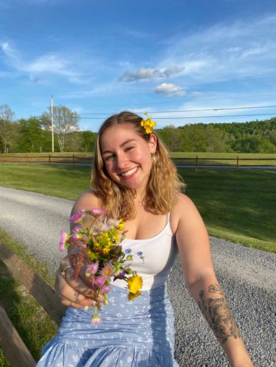 An image of Ashley holding out flowers in a rural setting
