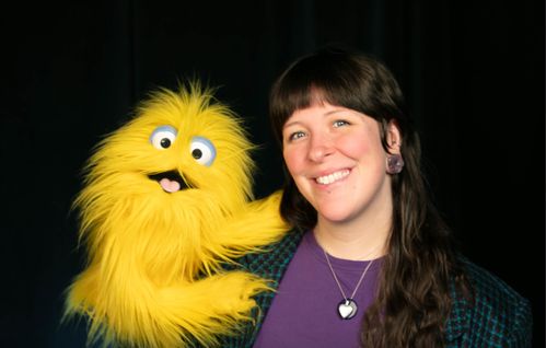 Chelsea Eliff headshot posing with a yellow, furry puppet