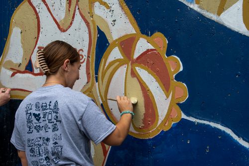 An art education student takes part in painting a mural on Beechurst Avenue