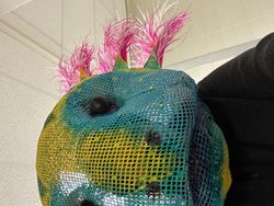 The face of a sequined puppet with pink feathers for hair 